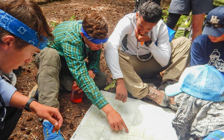 a group of people examine a map that is spread out on the ground